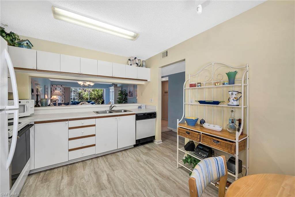 Kitchen featuring light countertops, white appliances, light wood finished floors, a textured ceiling, and two tone cabinets