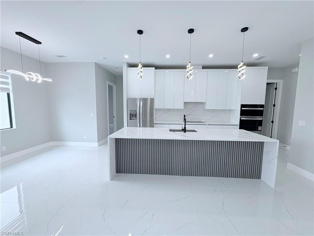 Kitchen with light stone counters, stainless steel appliances, white cabinetry, decorative light fixtures, and a large island