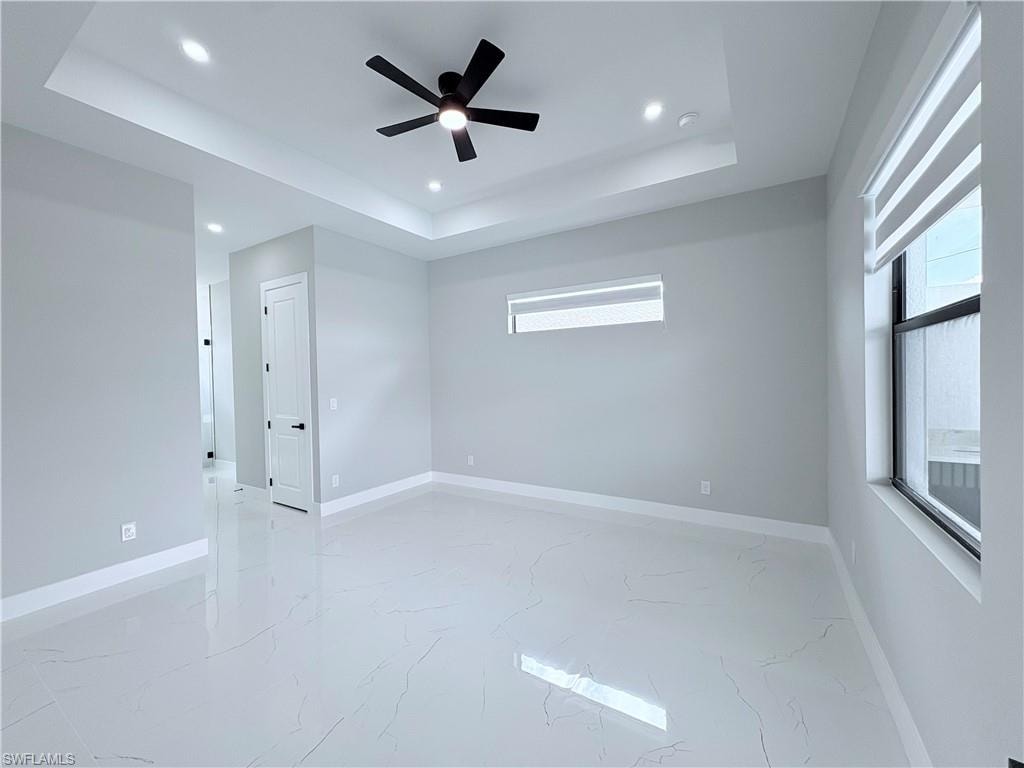 Spare room with plenty of natural light, ceiling fan, light marble finish floors, a raised ceiling, and recessed lighting