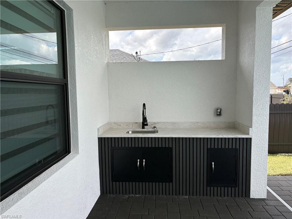 Bar area featuring a textured wall, light stone counters, and dark cabinets