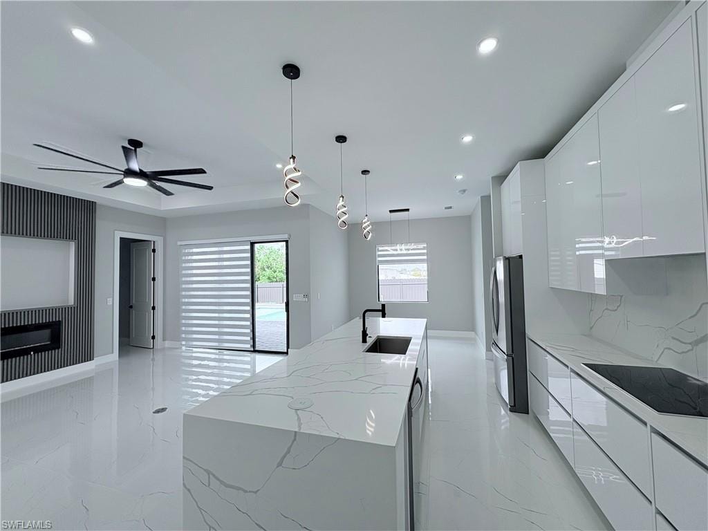 Kitchen featuring a kitchen island with sink, modern cabinets, black electric cooktop, and white cabinetry