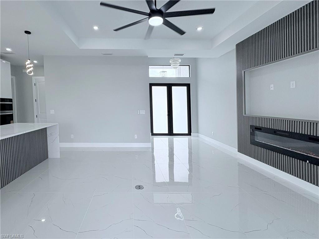 Empty room with light marble finish flooring, recessed lighting, a tray ceiling, a ceiling fan, and french doors