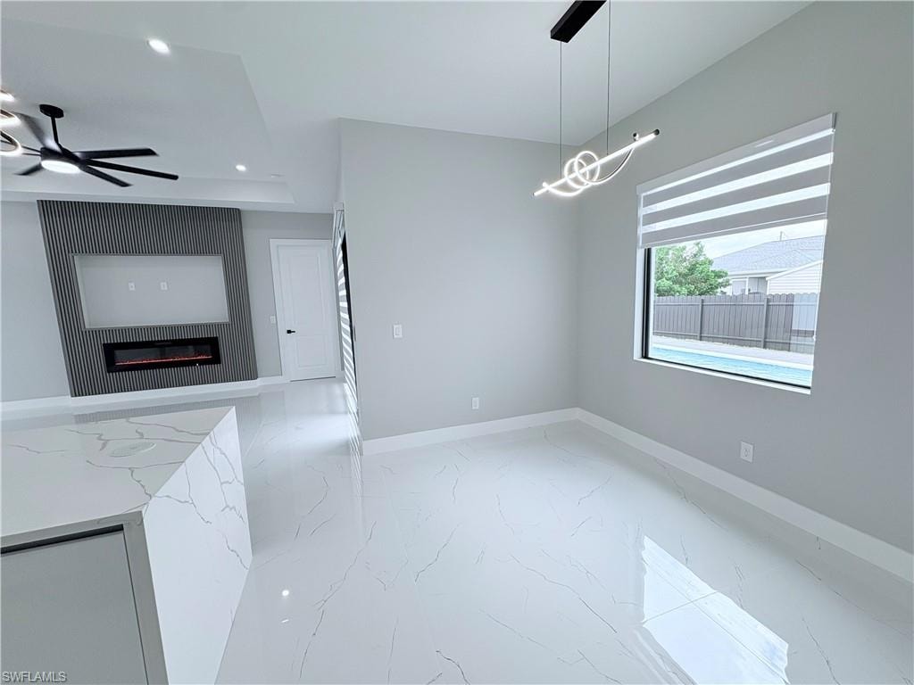 Unfurnished dining area with ceiling fan, a glass covered fireplace, light marble finish floors, and recessed lighting