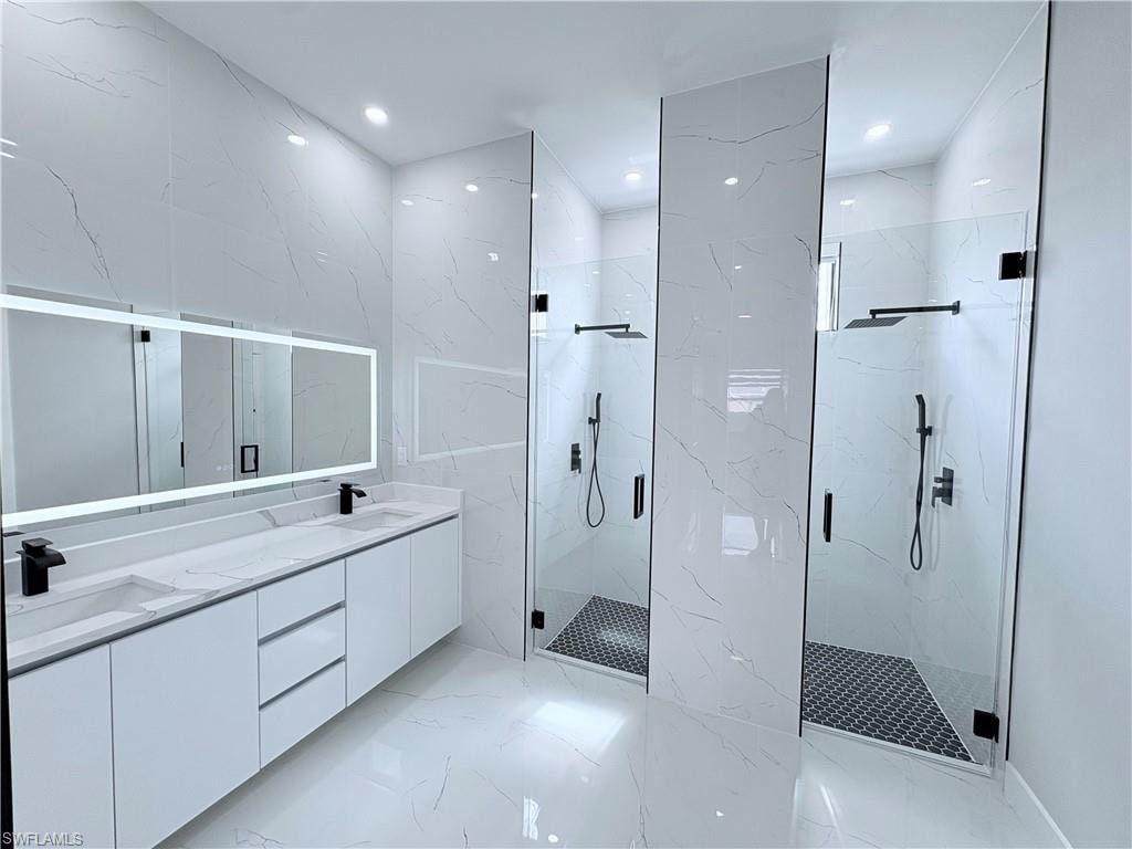 Bathroom featuring double vanity, a marble finish shower, recessed lighting, stone wall, and light marble finish flooring