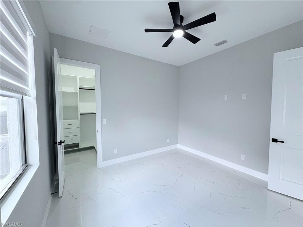 Unfurnished bedroom featuring a spacious closet, a ceiling fan, and light marble finish floors