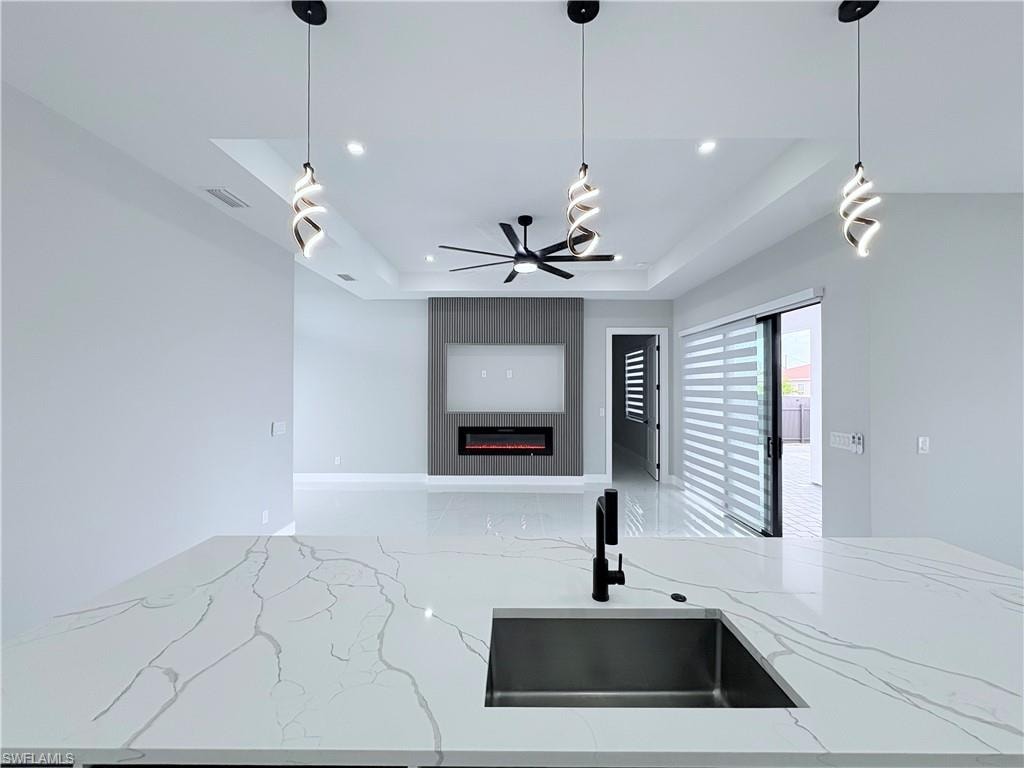 Kitchen with light stone countertops, a raised ceiling, a large fireplace, pendant lighting, and open floor plan