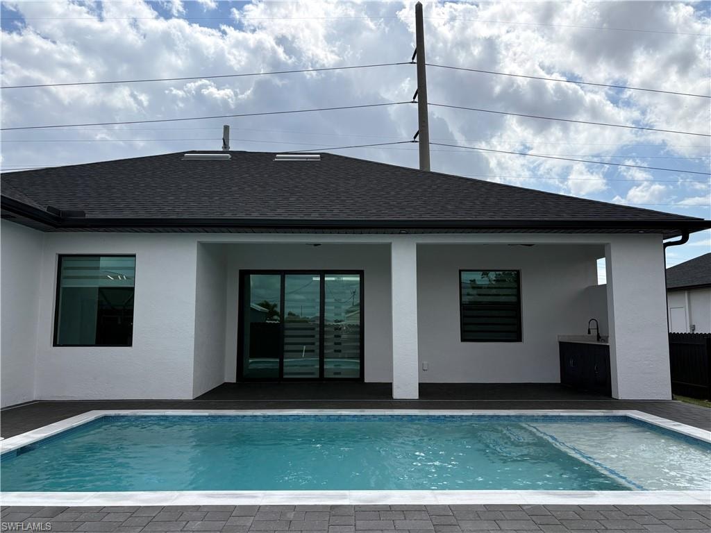 Back of property with a patio area, roof with shingles, an outdoor pool, and stucco siding