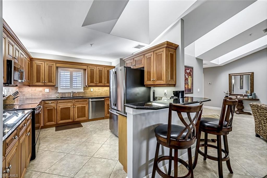 Kitchen with wood finish cabinetry, a kitchen bar, stainless steel appliances, light tile floors, and lofted ceiling