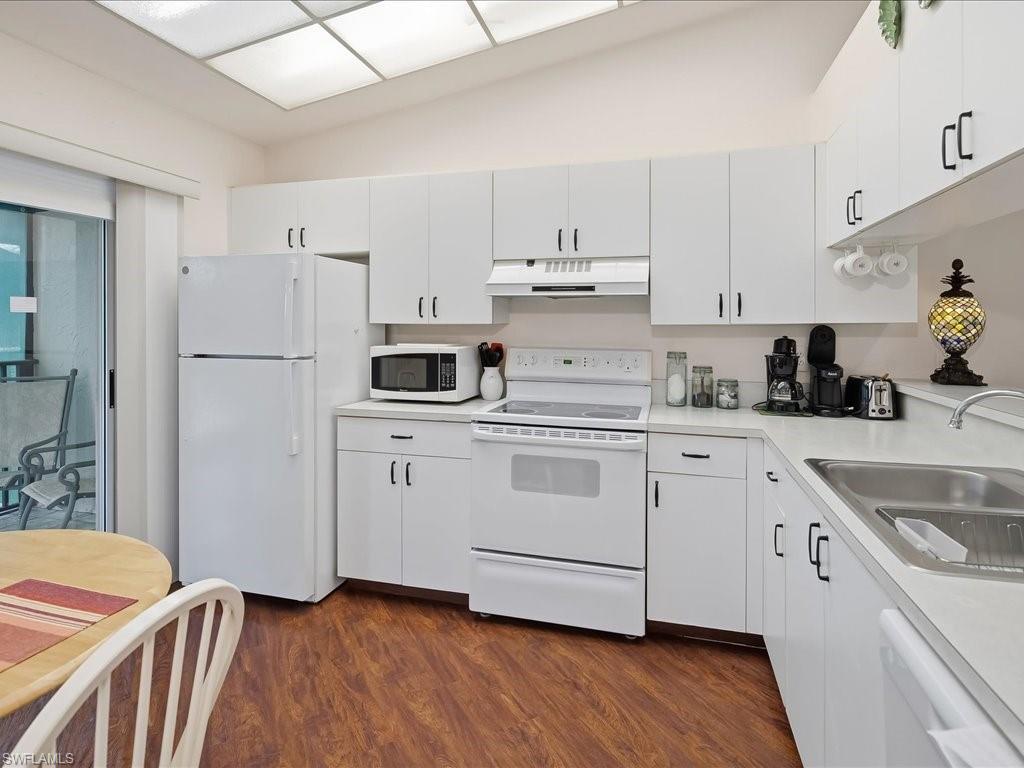 Kitchen featuring white appliances, white cabinets, light countertops, under cabinet range hood, and lofted ceiling