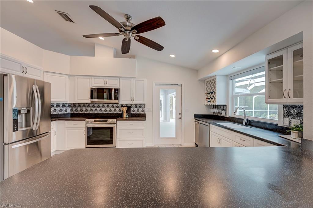 Kitchen with stainless steel appliances, dark countertops, backsplash, white cabinetry, and recessed lighting