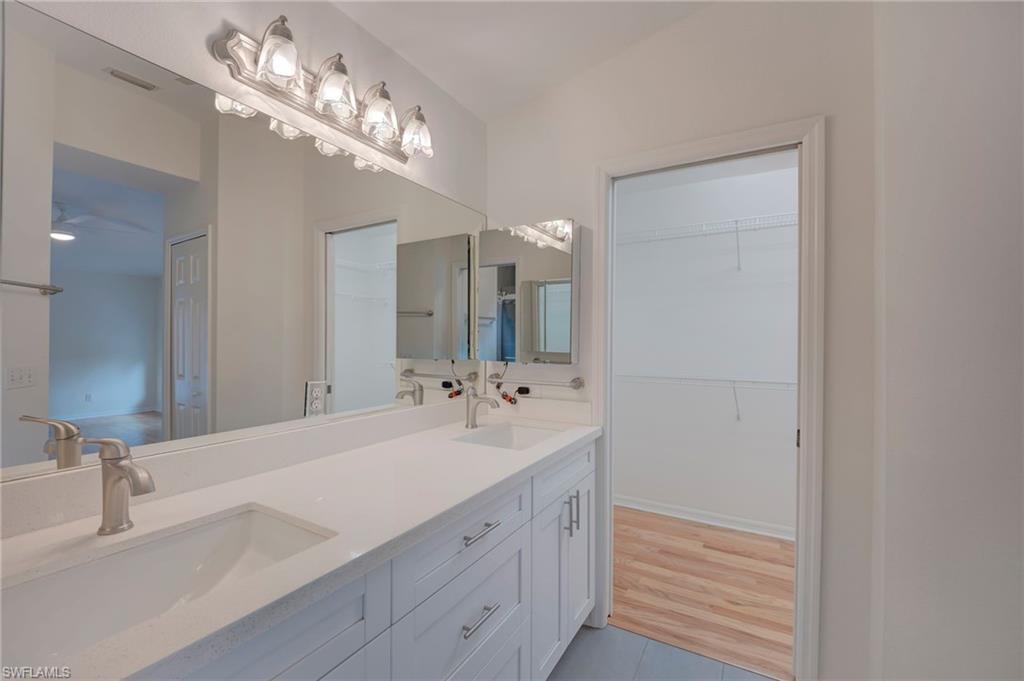 Full bath with double vanity, a spacious closet, and light wood-type flooring