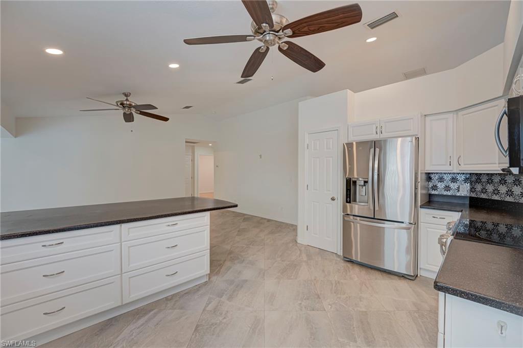 Kitchen with stainless steel appliances, ceiling fan, white cabinets, recessed lighting, and dark stone countertops