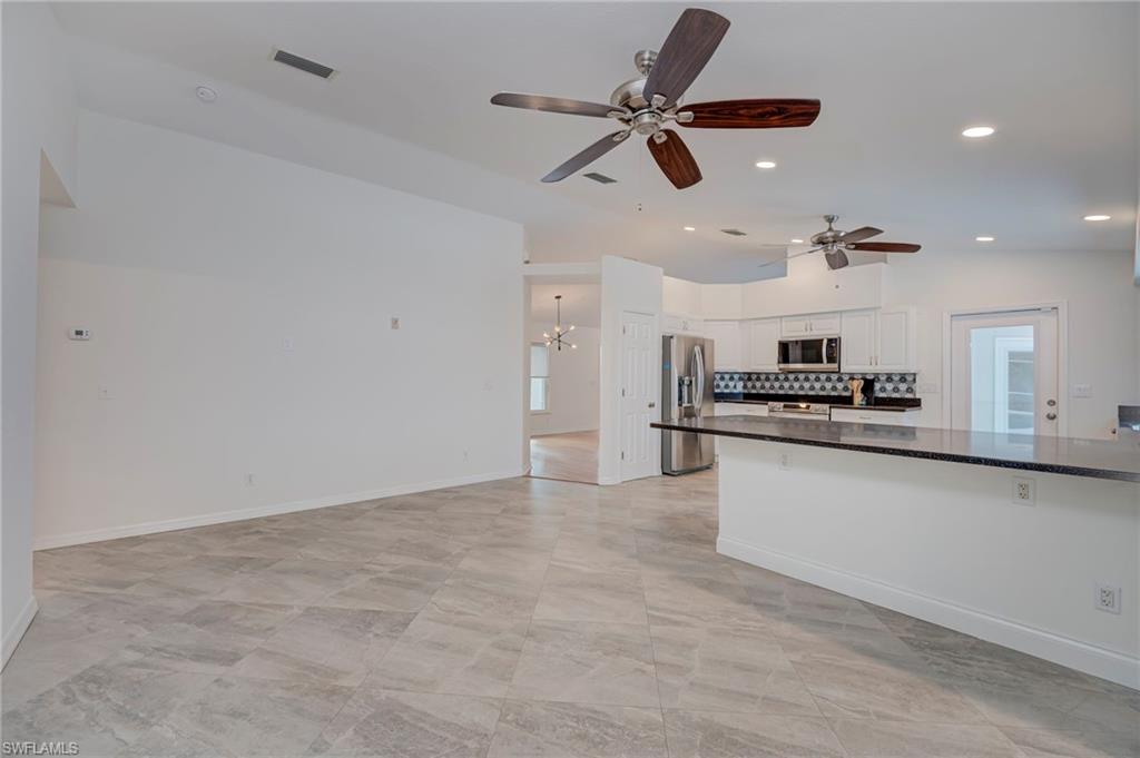 Kitchen featuring white cabinetry, stainless steel appliances, vaulted ceiling, a ceiling fan, and a chandelier