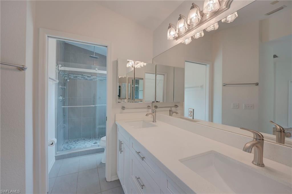 Full bath with a stall shower, double vanity, and light tile patterned flooring