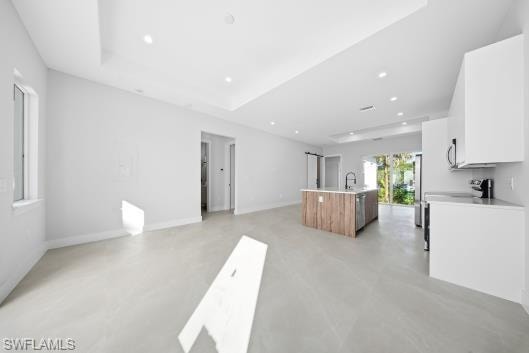 Two tone kitchen featuring a center island with sink, concrete flooring, open floor plan, recessed lighting, and a raised ceiling