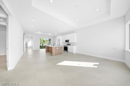 Kitchen featuring open floor plan, light countertops, a center island with sink, stainless steel appliances, and dual tone cabinetry