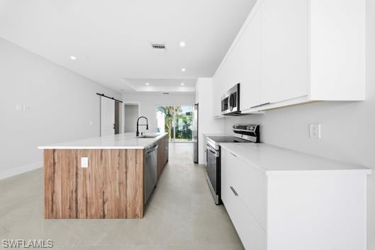 Kitchen with a spacious island, stainless steel appliances, finished concrete floors, a barn door, and two tone cabinets