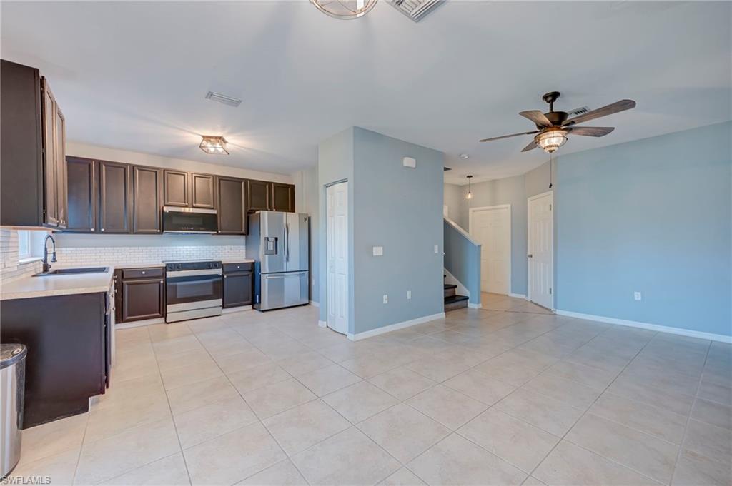 Kitchen featuring dark wood finish cabinetry, stainless steel appliances, tasteful backsplash, light tile patterned floors, and a ceiling fan