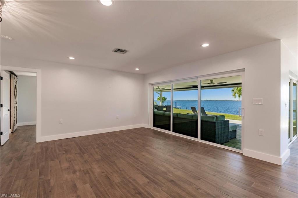Empty room featuring a water view, visible vents, dark wood finished floors, and recessed lighting
