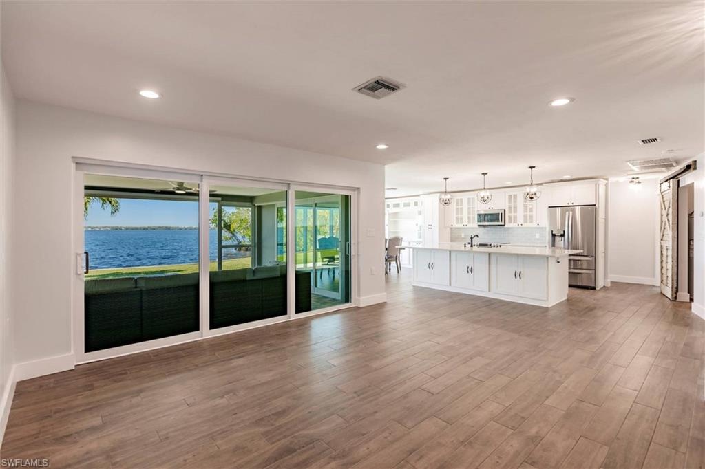 Unfurnished living room featuring baseboards, visible vents, dark wood-type flooring, a water view, and recessed lighting