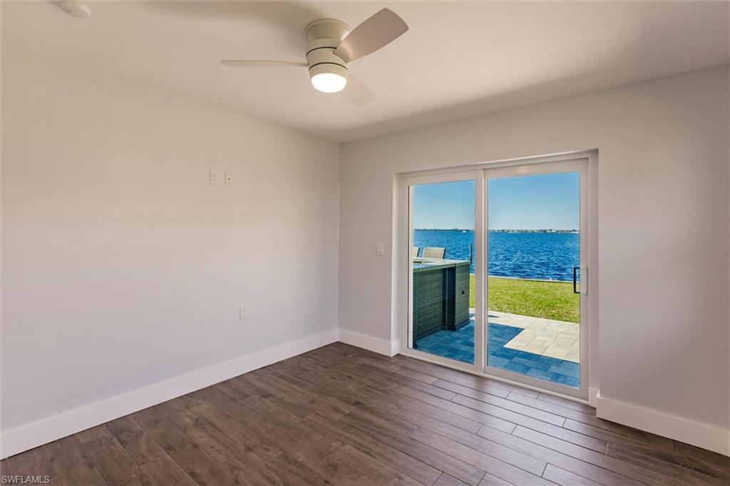 Spare room with dark wood-style flooring, a water view, a ceiling fan, and baseboards