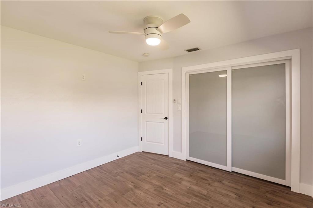 Unfurnished bedroom with dark wood-style flooring, a ceiling fan, visible vents, baseboards, and a closet