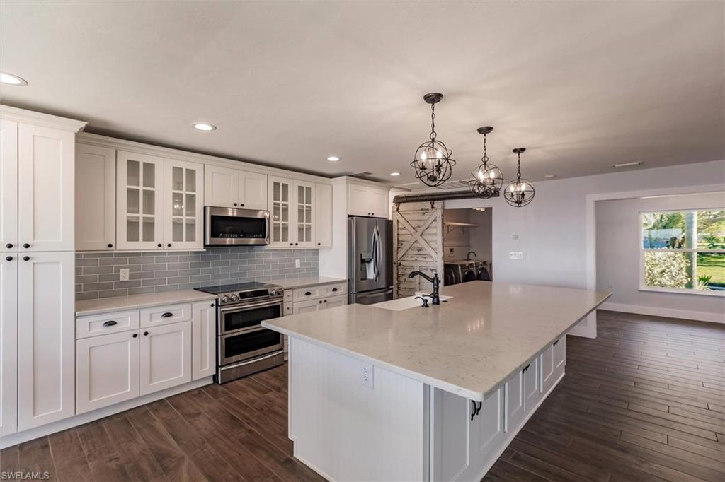 Kitchen with stainless steel appliances, a sink, white cabinets, an island with sink, and glass insert cabinets