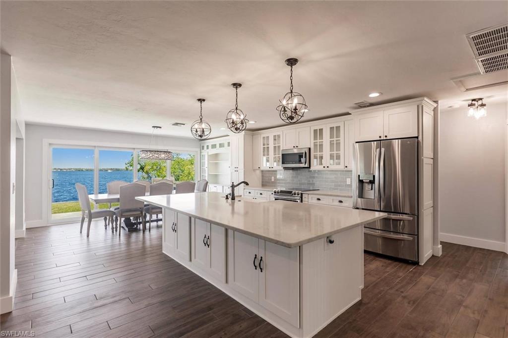 Kitchen featuring appliances with stainless steel finishes, glass insert cabinets, a water view, a kitchen island with sink, and light countertops