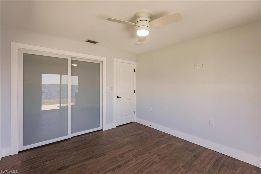 Unfurnished room featuring dark wood-style floors, visible vents, ceiling fan, and baseboards