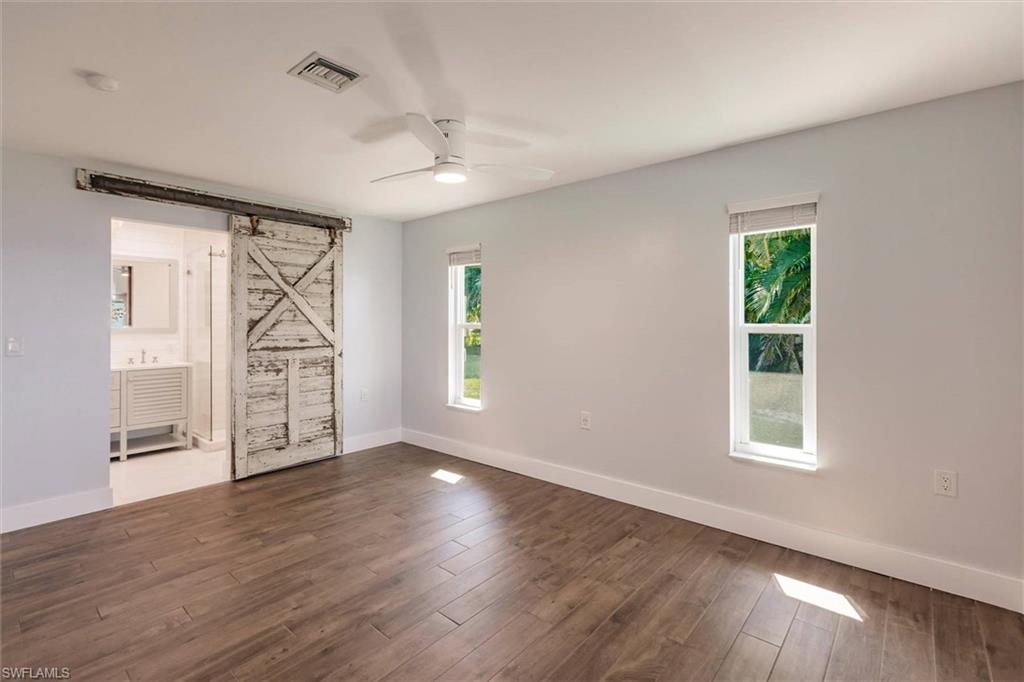 Spare room featuring a barn door, dark wood-type flooring, a ceiling fan, and baseboards