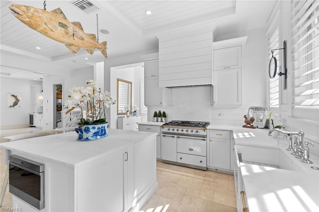 Kitchen with white cabinetry, double oven range, backsplash, stone tile flooring, and stainless steel microwave