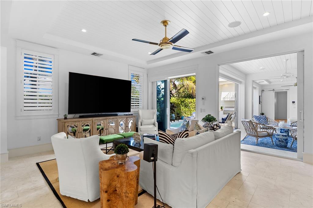 Living room with ceiling fan, a wooden tray ceiling, recessed lighting, and light stone finish floors