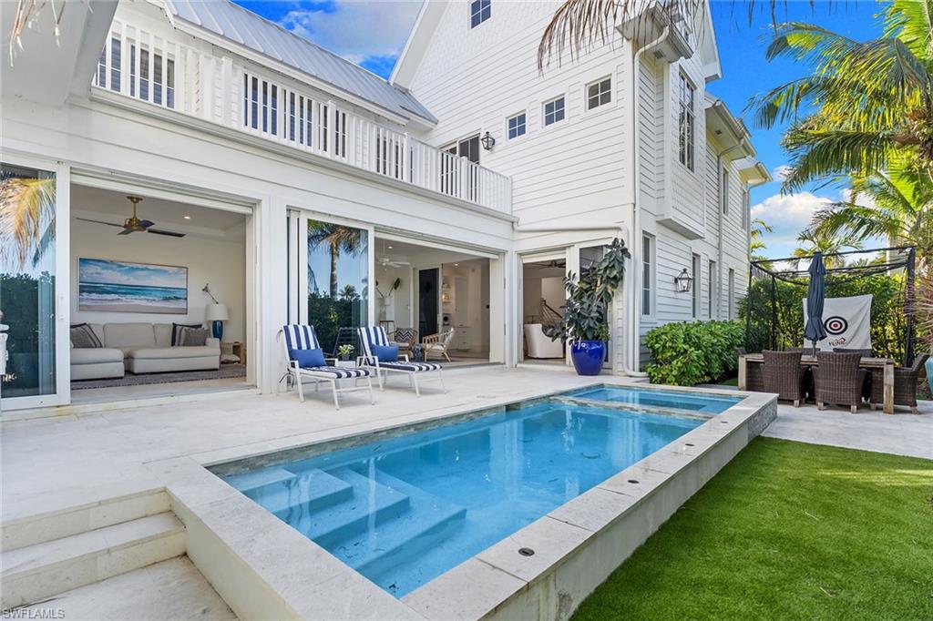 Back of house with a patio area, outdoor dining area, a metal roof, a balcony, and a pool with connected hot tub