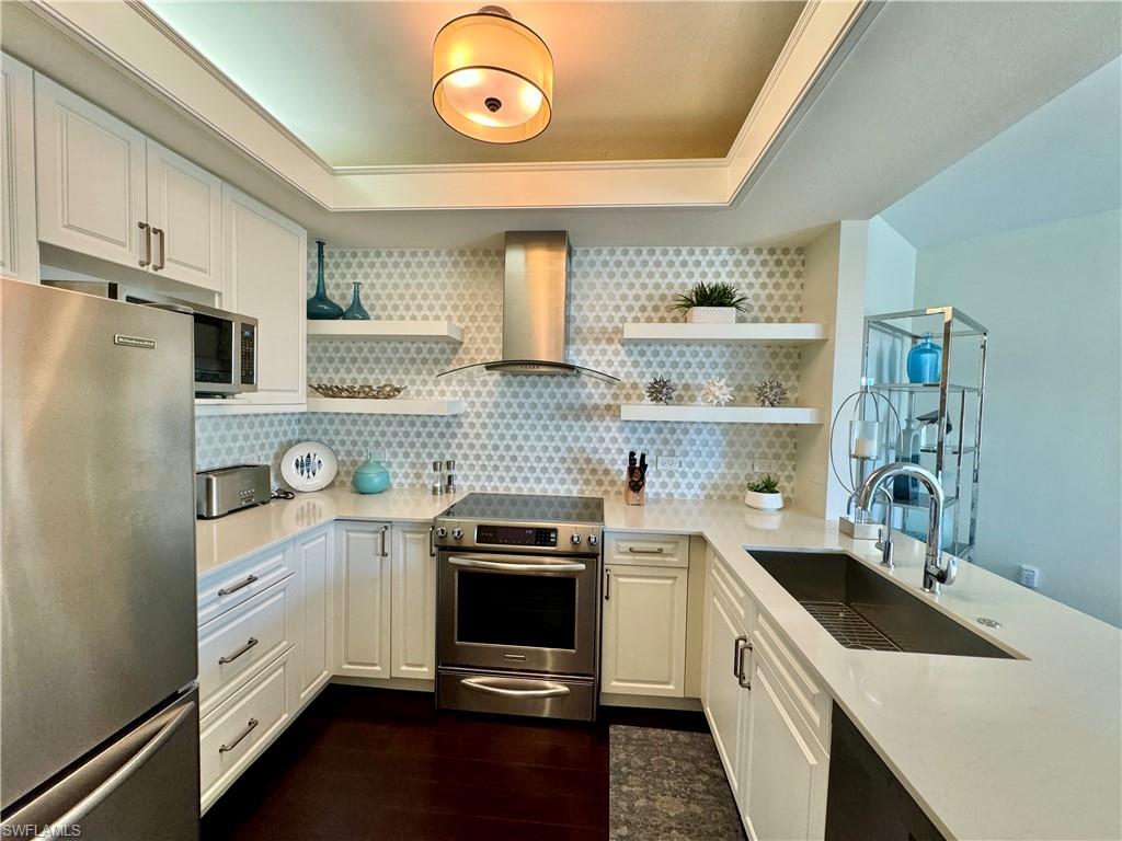 Kitchen with white cabinetry, stainless steel appliances, wall chimney exhaust hood, and sink
