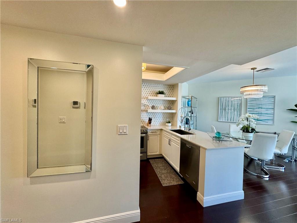 Kitchen with kitchen peninsula, stainless steel appliances, sink, decorative light fixtures, and white cabinets