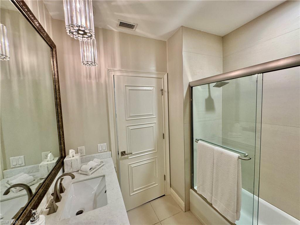 Bathroom with a shower with door, vanity, an inviting chandelier, and tile patterned flooring