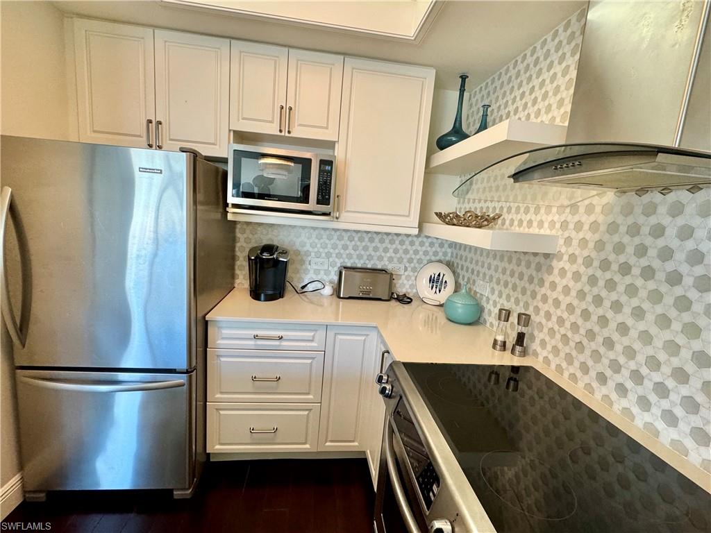 Kitchen with wall chimney range hood, white cabinetry, and stainless steel appliances