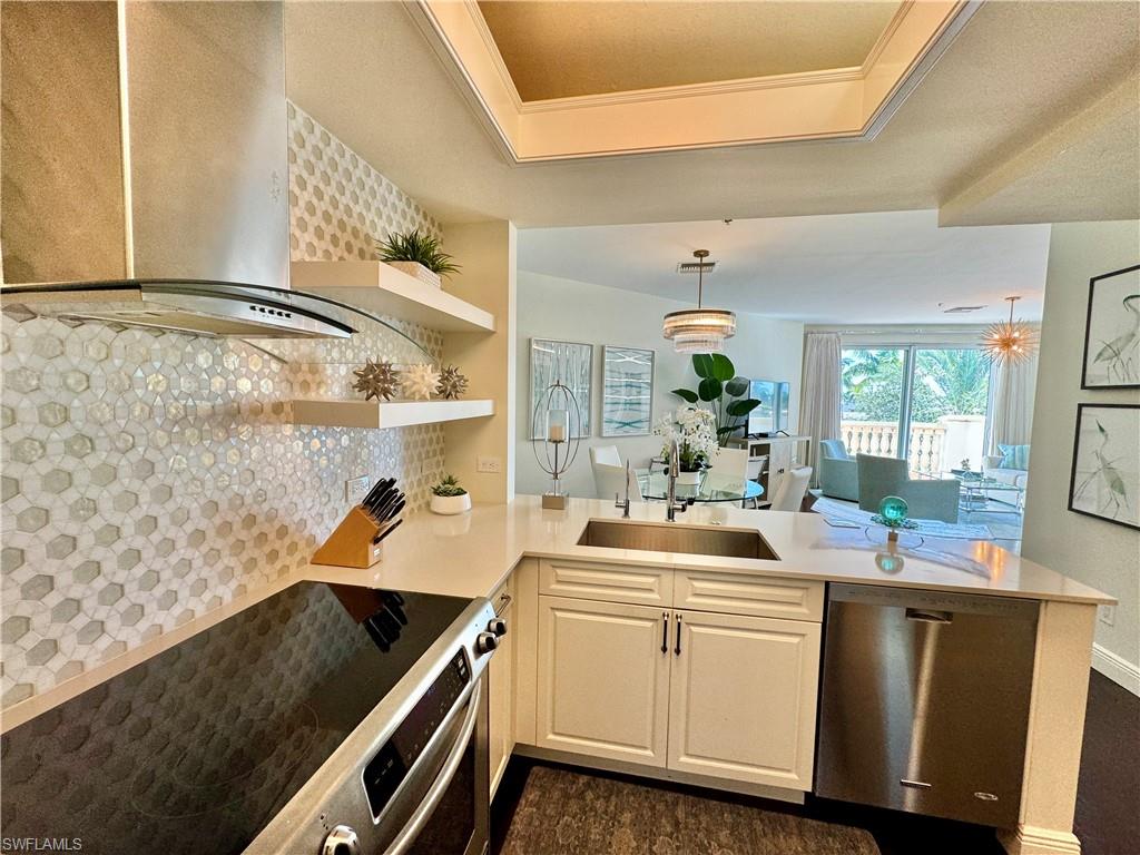 Kitchen with wall chimney range hood, hanging light fixtures, stainless steel appliances, kitchen peninsula, and sink