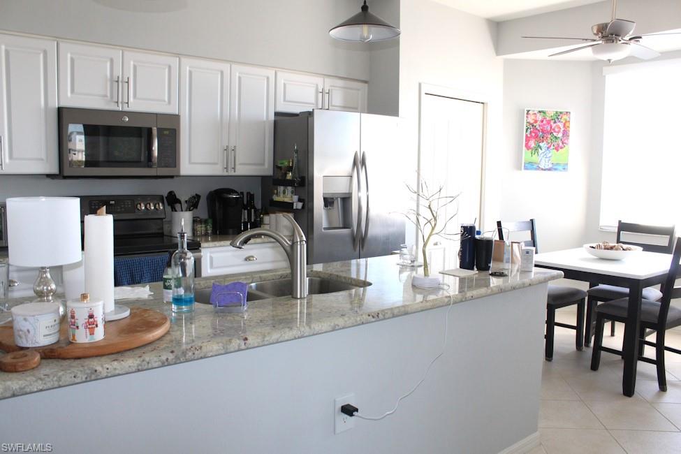 Kitchen with stainless steel appliances, light stone counters, white cabinetry, ceiling fan, and pendant lighting
