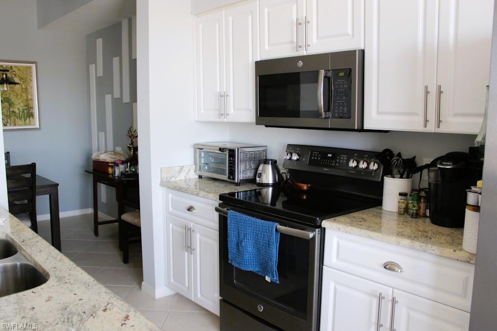 Kitchen featuring black range with electric stovetop, stainless steel microwave, white cabinets, and light stone countertops