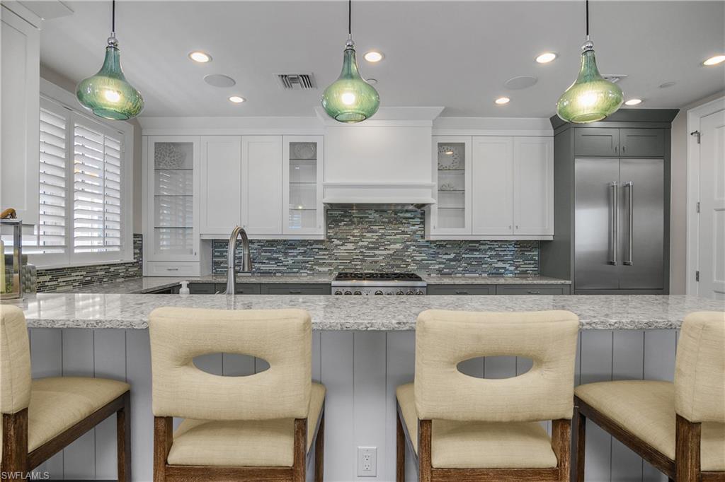 Kitchen featuring a breakfast bar area, decorative light fixtures, light stone counters, stainless steel appliances, and decorative backsplash