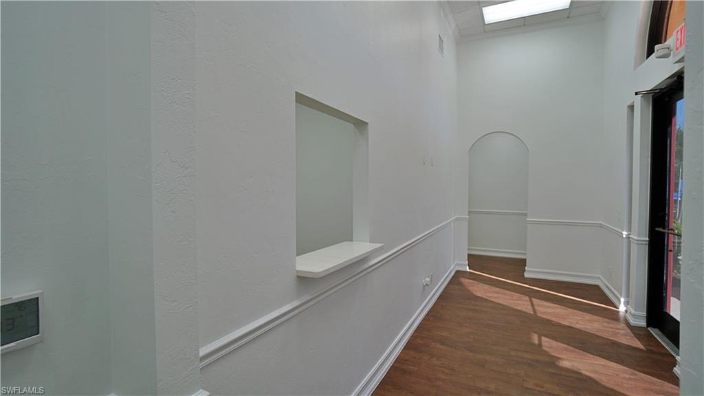 Hall with arched walkways, dark wood-style flooring, a high ceiling, and a textured wall