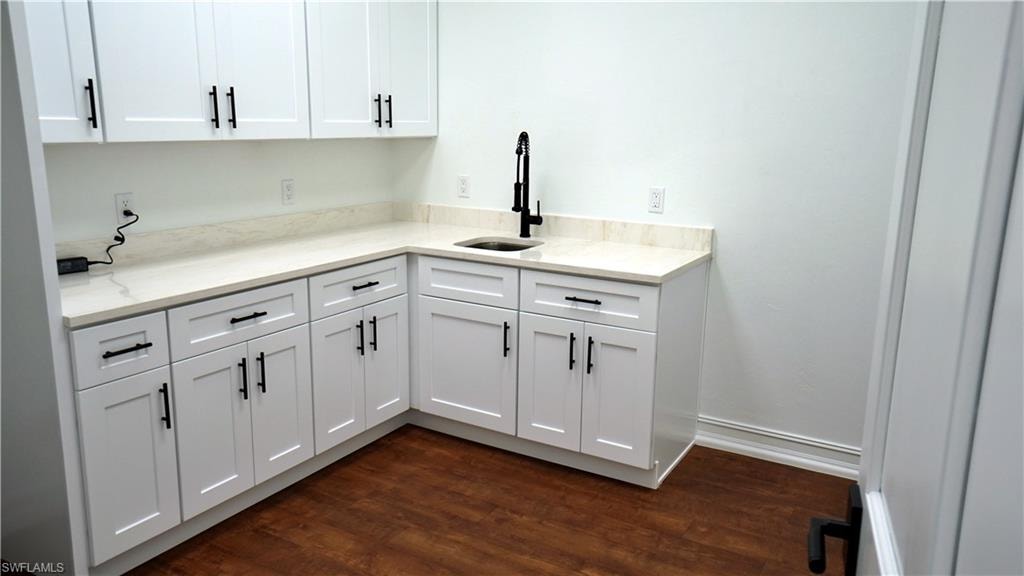 Kitchen with light stone countertops, dark wood finished floors, and white cabinetry