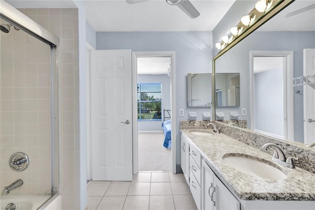 Ensuite bathroom featuring double vanity, a ceiling fan, light tile patterned flooring, and combined bath / shower with glass door
