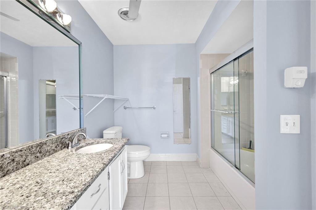 Bathroom with vanity, light tile patterned floors, and bath / shower combo with glass door