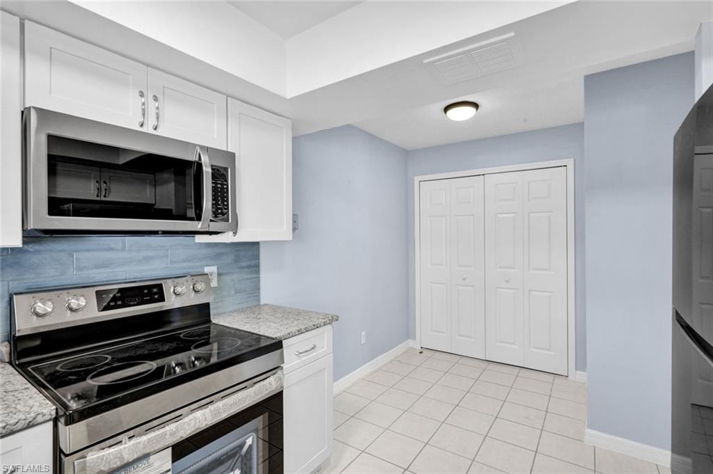 Kitchen with stainless steel appliances, white cabinets, light tile patterned floors, light stone countertops, and tasteful backsplash