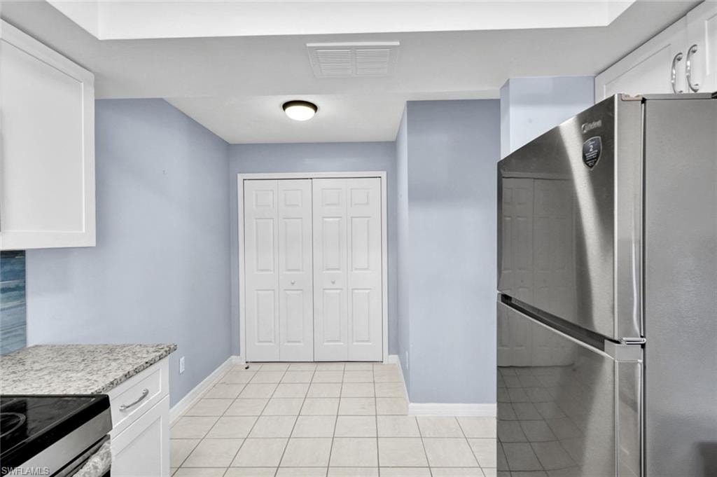 Kitchen featuring freestanding refrigerator, white cabinets, light stone countertops, range with electric cooktop, and light tile patterned floors