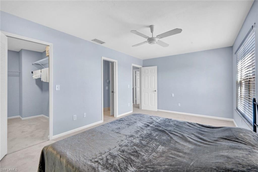 Bedroom featuring light carpet, a walk in closet, and ceiling fan