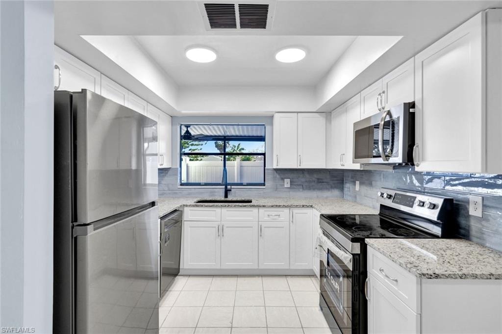 Kitchen featuring stainless steel appliances, light stone counters, white cabinetry, a raised ceiling, and light tile patterned floors