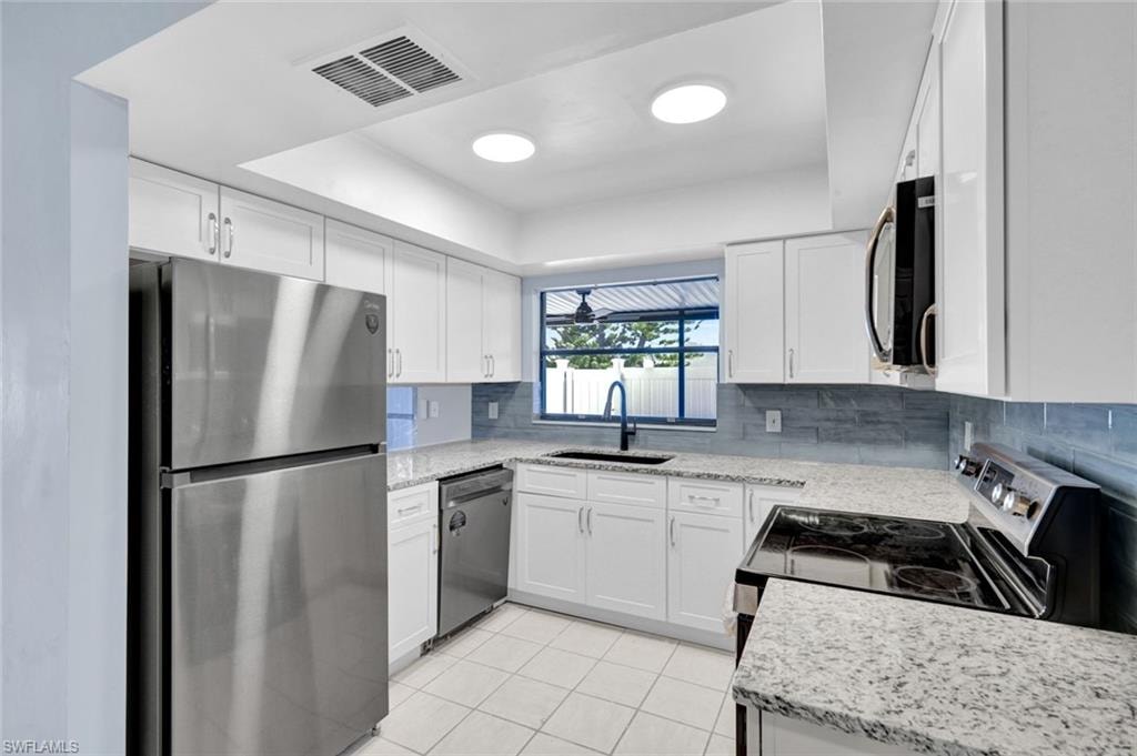 Kitchen featuring a raised ceiling, stainless steel appliances, light stone countertops, and white cabinets